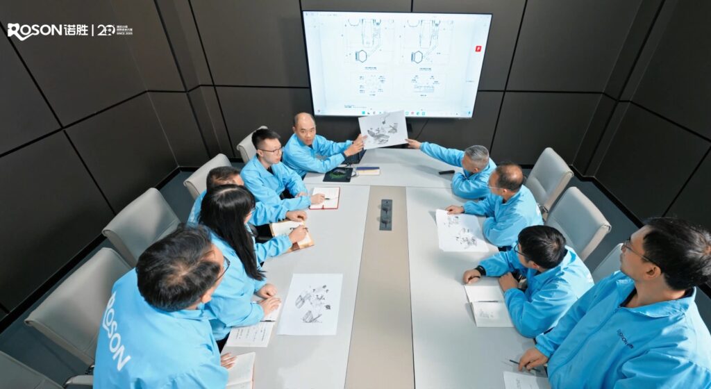 ROSON R&D team brainstorming dental innovation, reviewing detailed technical drawings in a conference room setting.